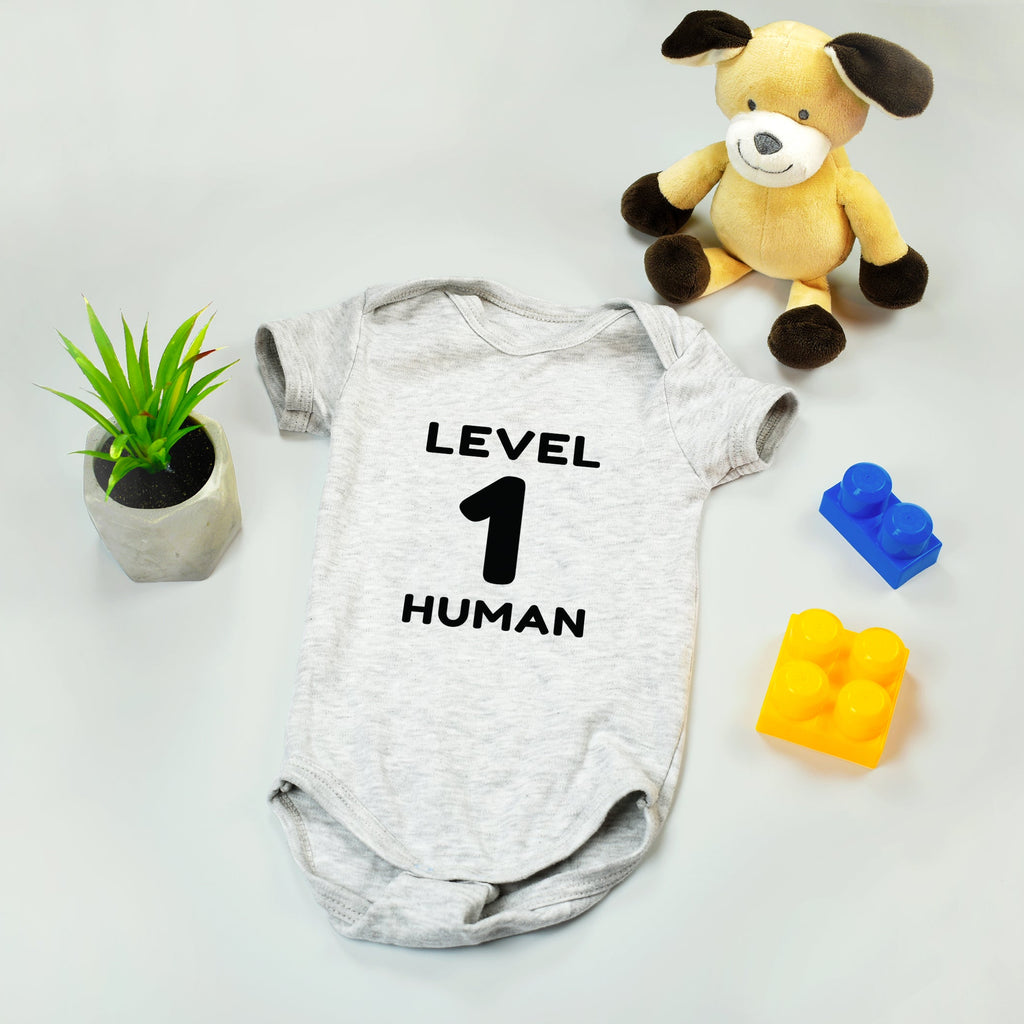 Baby onesie with 'Level 1 Human' text, plush toy, and colorful blocks on a light background