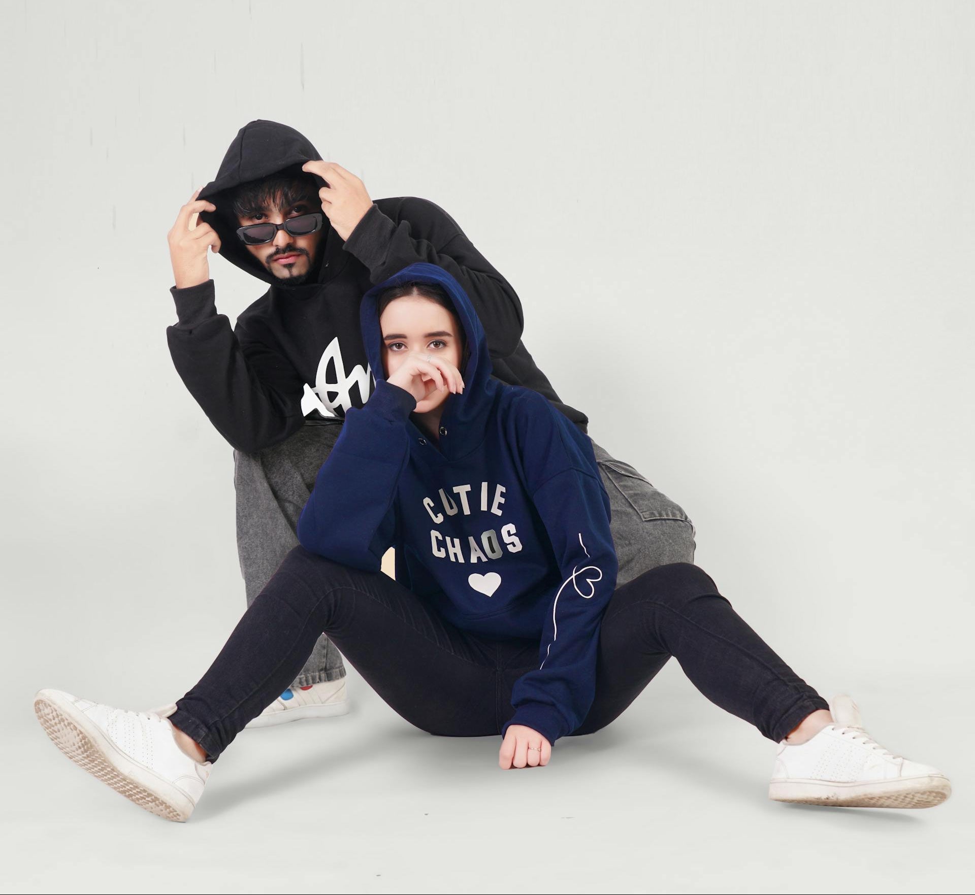 Two people wearing hoodies sitting on a light gray background