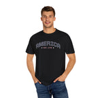 a man wearing a black t-shirt with 'AMERICA EST. 1776' typography design in varsity style on a white background