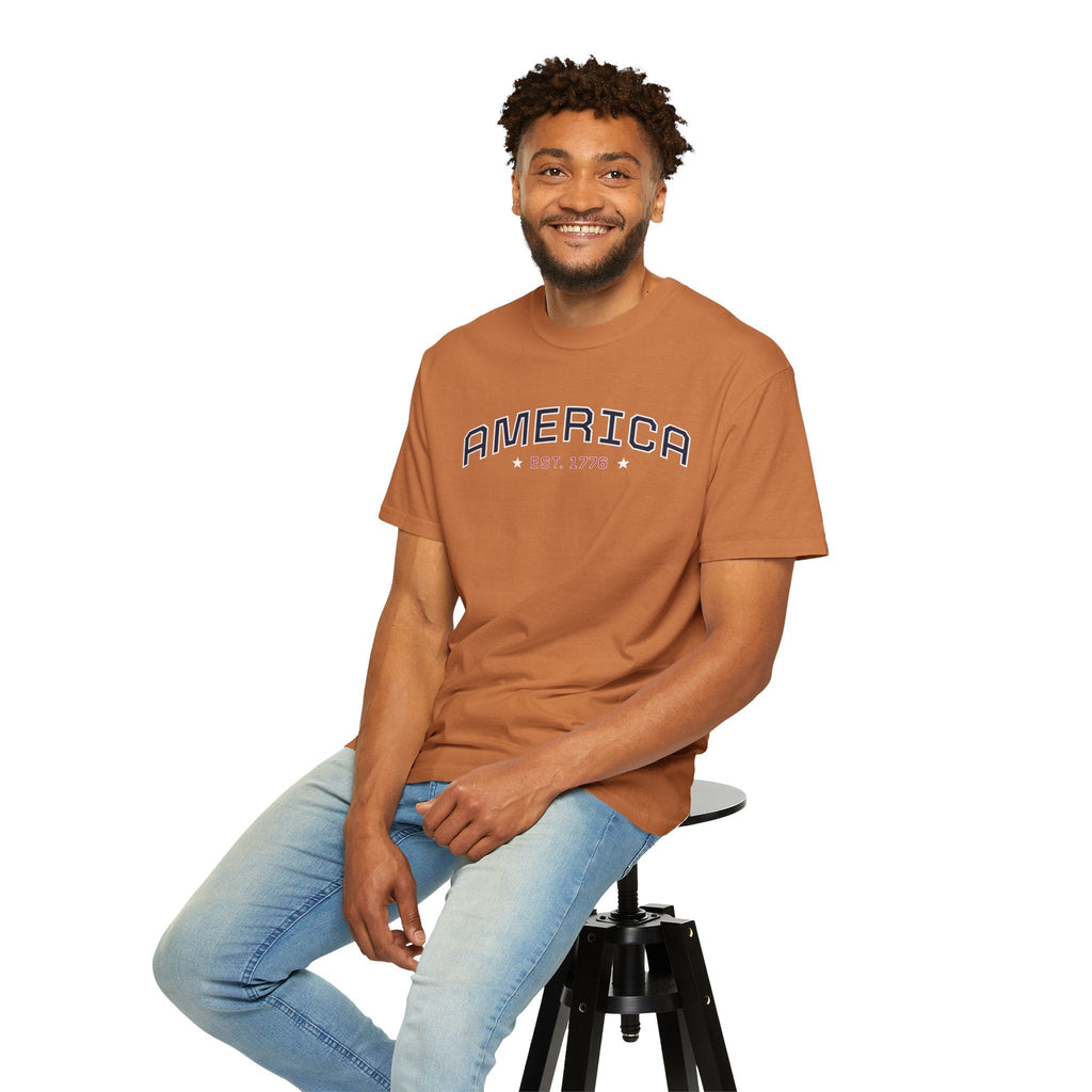 a man wearing a yam t-shirt with 'AMERICA EST. 1776' typography design in varsity style on a white background