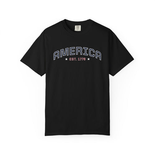 Black t-shirt with 'AMERICA EST. 1776' typography design in varsity style on a white background