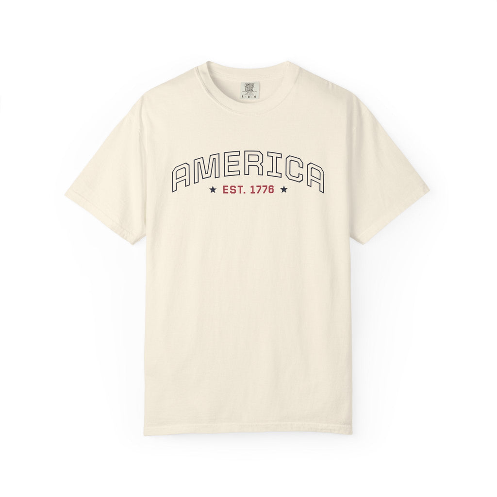 Ivory t-shirt with 'AMERICA EST. 1776' typography design in varsity style on a white background