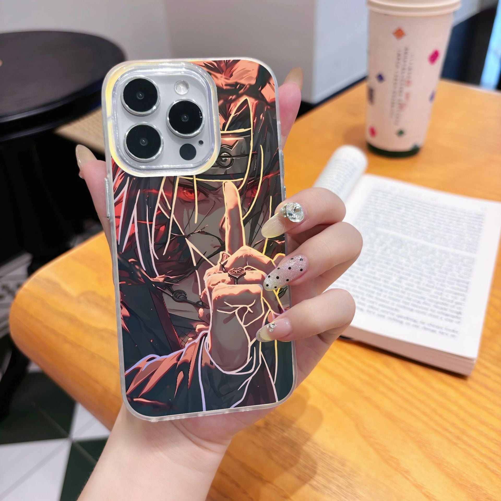 Hand holding a phone case with anime Naruto Shippuden Uchiha Itachi artistic design on a wooden table.