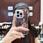 Person holding a phone with an anime Naruto Shippuden Uchiha Itachi design case in a blurred indoor setting