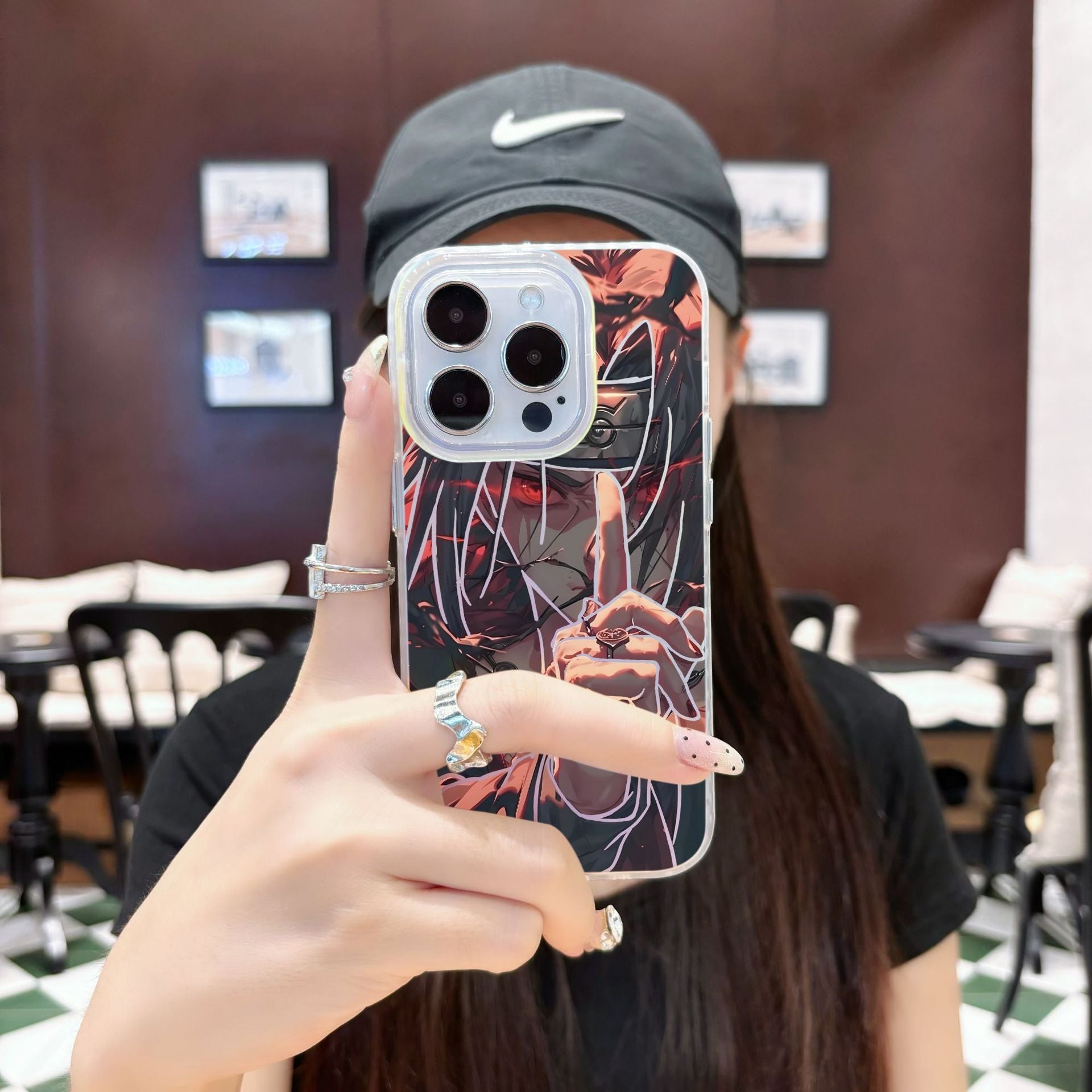 Person holding a phone with an anime Naruto Shippuden Uchiha Itachi design case in a blurred indoor setting