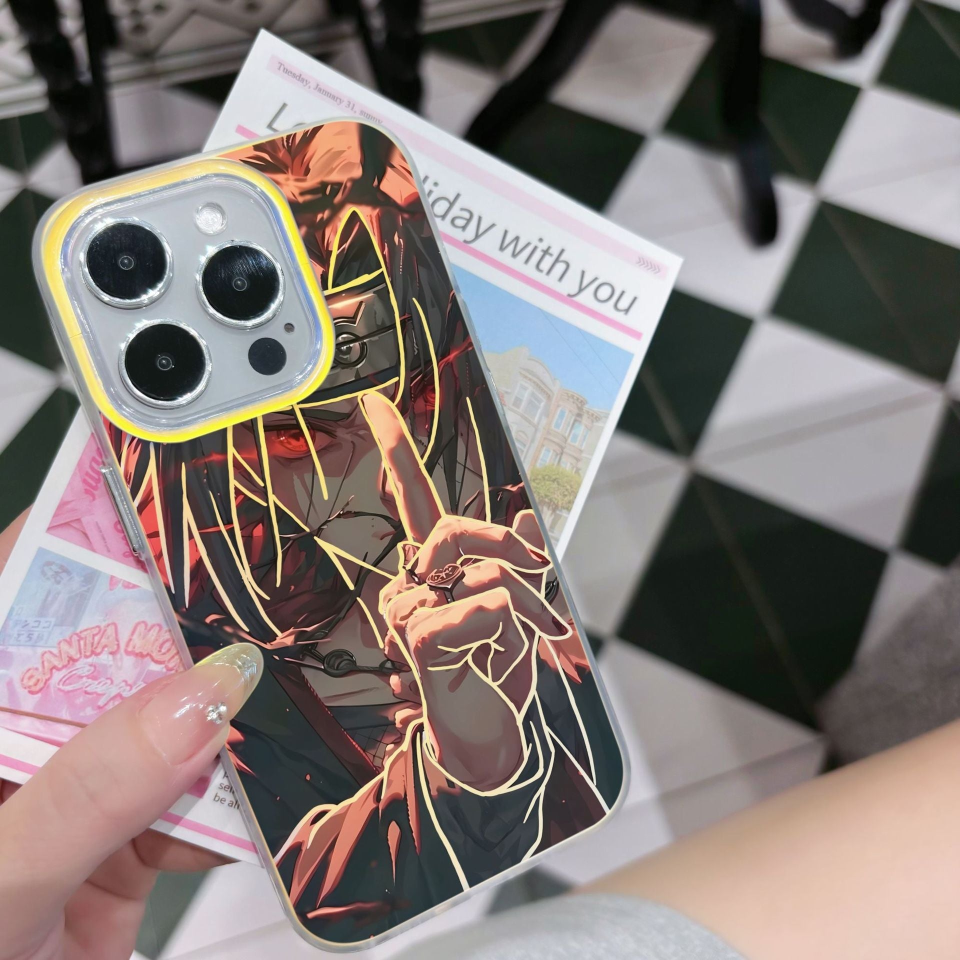 Phone case with anime Naruto Shippuden Uchiha Itachi artistic design held by a person on a checkered floor.
