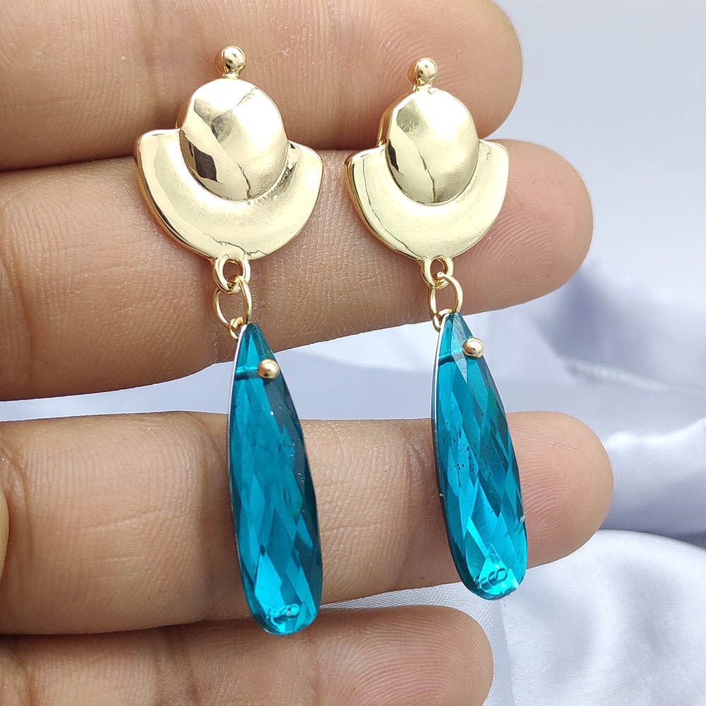 Gold earrings with blue teardrop-shaped stones held between fingers against a neutral background