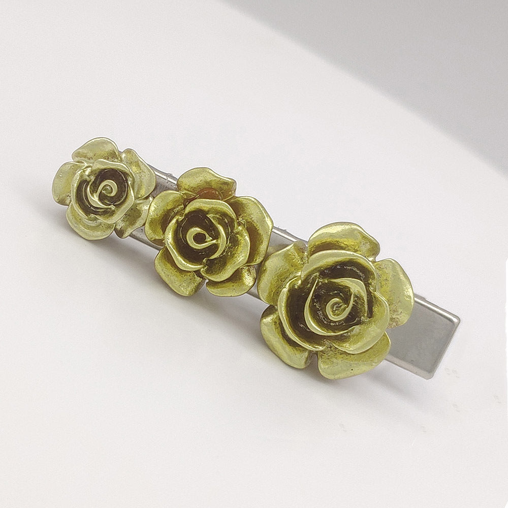 Hair clip with three gold rose flowers on a white background