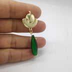 Gold earrings with green teardrop-shaped stones on a hand against a white background