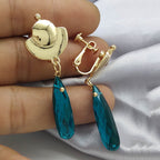 Gold earrings with blue teardrop-shaped stones on a hand against a light fabric background
