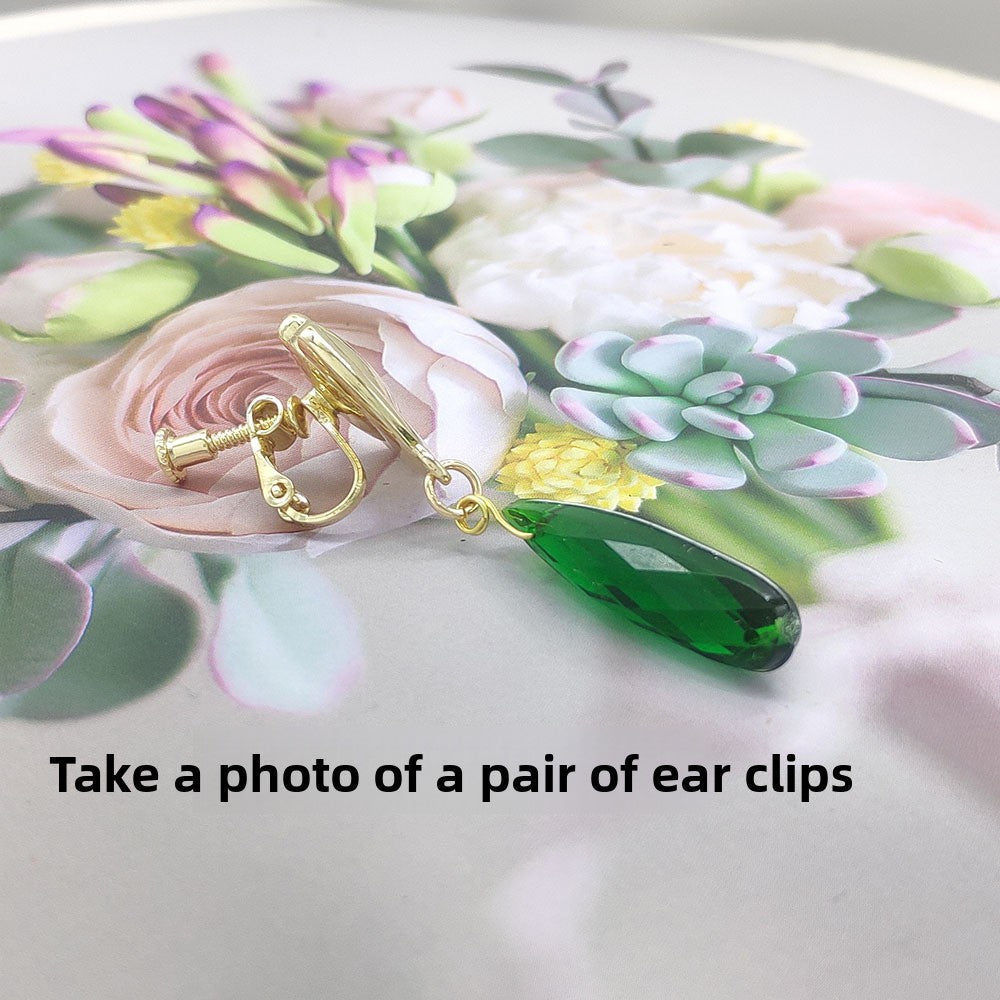 Gold ear clip with green teardrop charm on a floral background