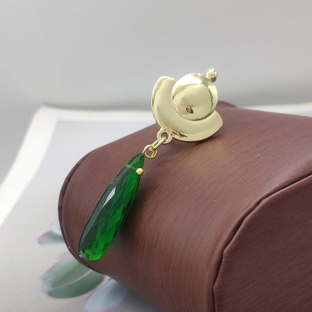 Gold earring with a green teardrop-shaped gemstone on a brown cushion