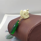 Gold earring with a green teardrop-shaped gemstone on a brown cushion
