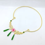 Gold necklace with green beads and a pink flower pendant on a white background