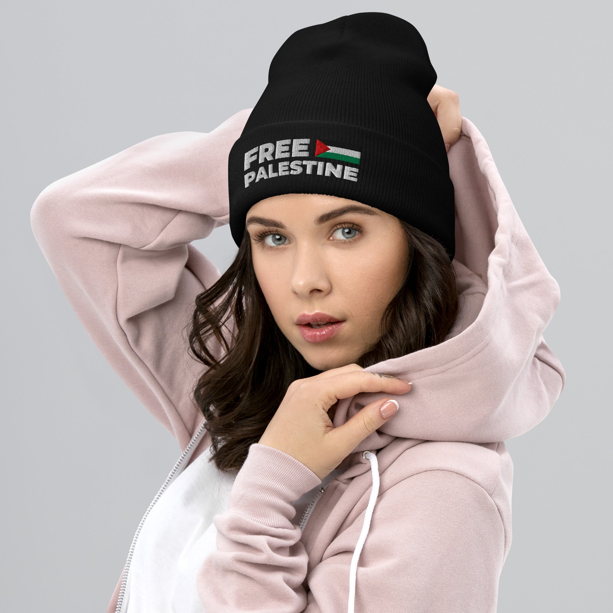 Person wearing a black beanie with 'Free Palestine' text and a flag design, over a pink hoodie.