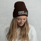 Person wearing a black beanie with 'Free Palestine' text and flag design against a light gray background