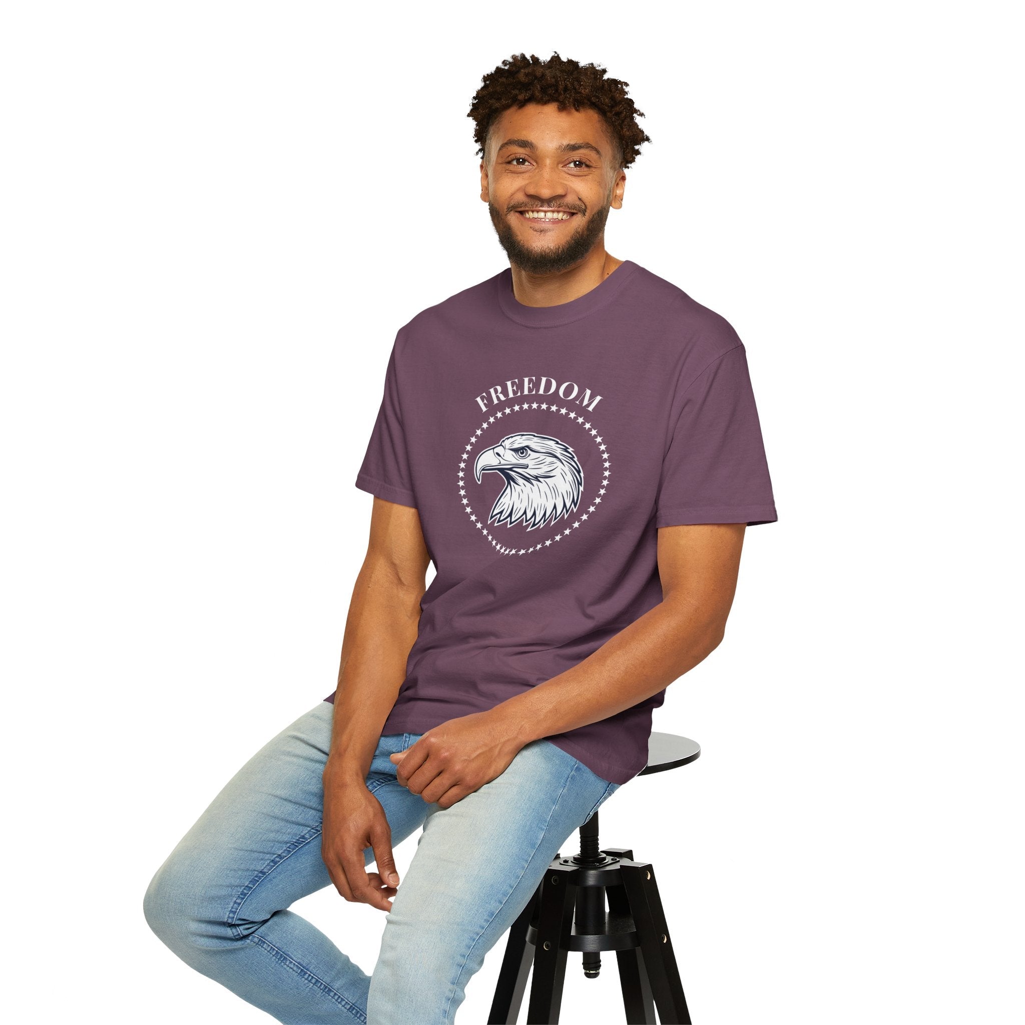 a man sitting on a chair, wearing a berry color t-shirt with the eagle freedom and starts graphic design on a white background.