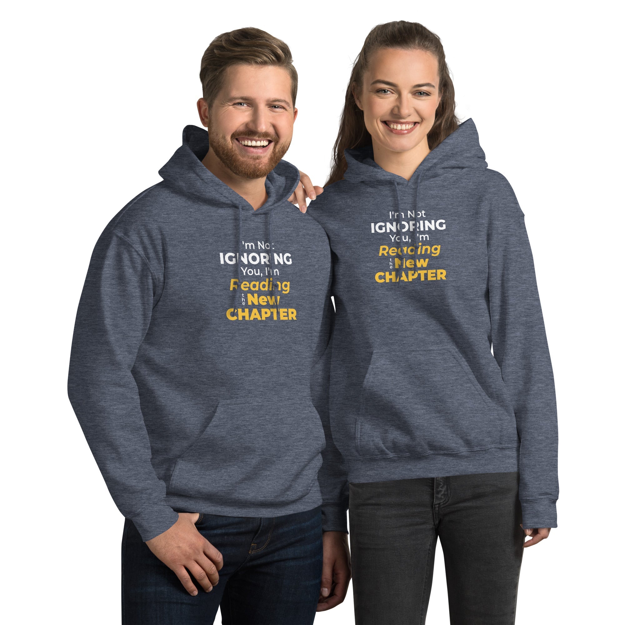 Two people wearing matching blue hoodies with humorous 'I'm Not Ignoring You, I'm Reading the New Chapter' text on a white background