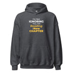 Dark gray hoodie with humorous 'I'm Not Ignoring You, I'm Reading the New Chapter' text design on a white background