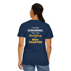 A woman wearing black t-shirt with text 'I'm Not Ignoring You, I'm Reading the New Chapter' on the back side on a white background