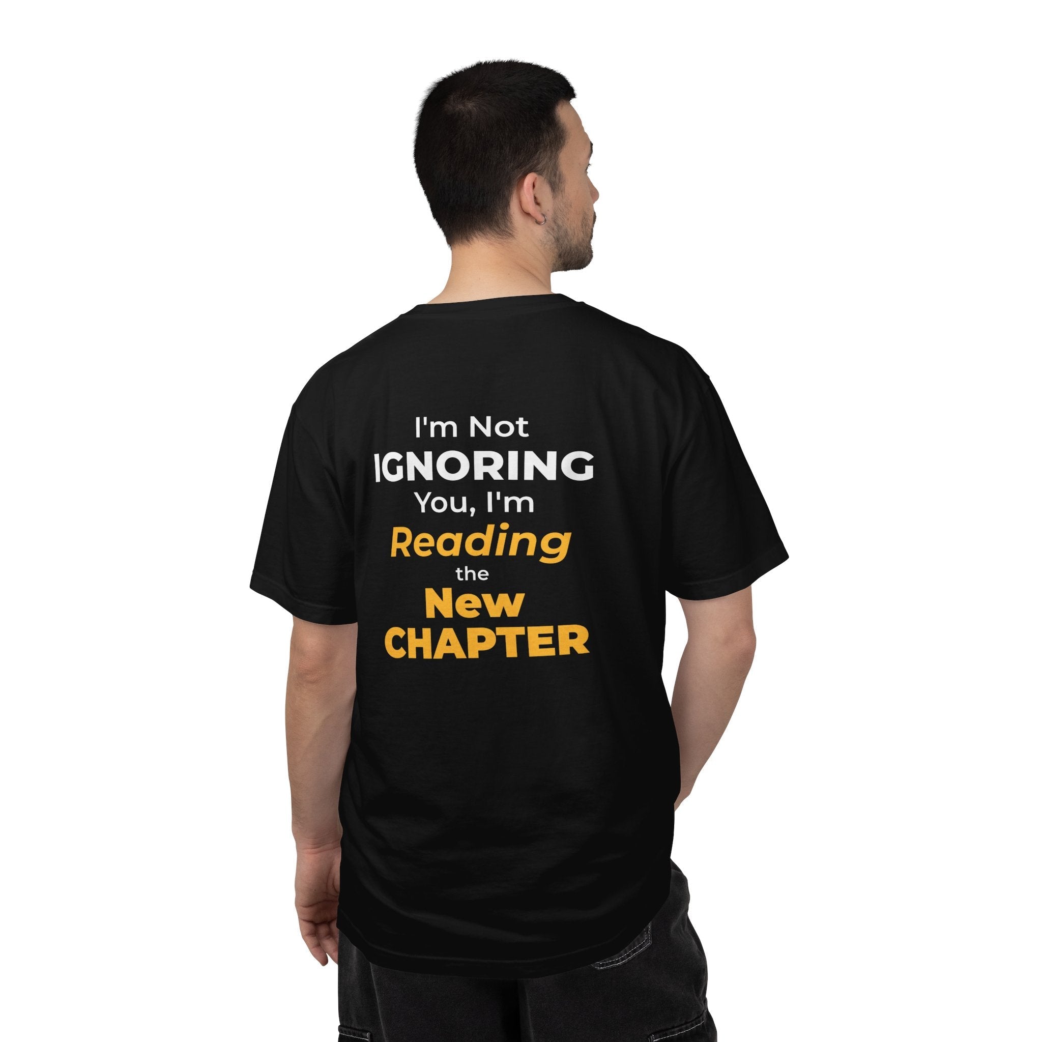 A man wearing black t-shirt with text 'I'm Not Ignoring You, I'm Reading the New Chapter' on the back side on a white background