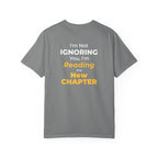 Grey t-shirt with text 'I'm Not Ignoring You, I'm Reading the New Chapter' on the back side on a white background