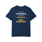 Navy t-shirt with text 'I'm Not Ignoring You, I'm Reading the New Chapter' on the back side on a white background