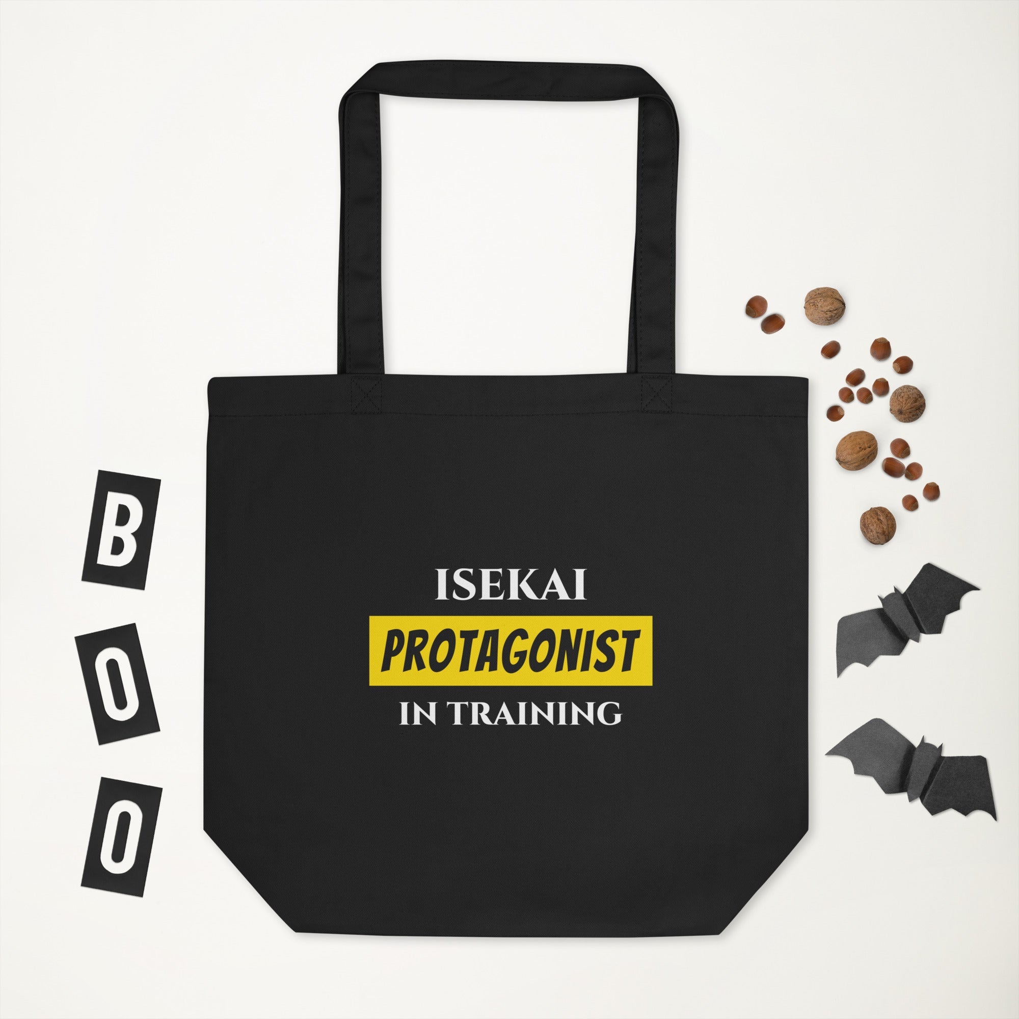Black tote bag with 'Isekai Protagonist in Training' text, surrounded by Halloween-themed items on a white background.