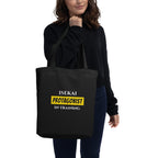 Person holding a black tote bag with 'ISEKAI PROTAGONIST IN TRAINING' text.