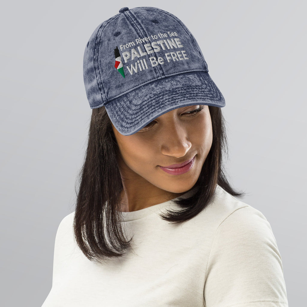 Person wearing a blue cap with text and a Palestine flag design on a gray background