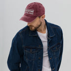 A man wearing a denim jacket and a maroon cap with the text and Palestine flag, on a plain background