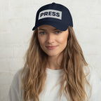 Woman wearing a navy blue cap with 'PRESS' on a white background