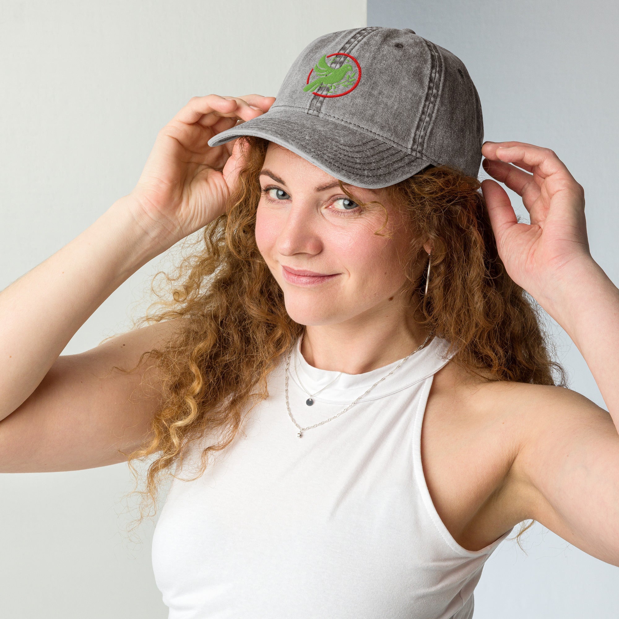 A Woman wearing a gray cap with a bird logo, posing against a plain background