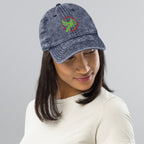 Person wearing a blue denim cap with a logo on a gray background