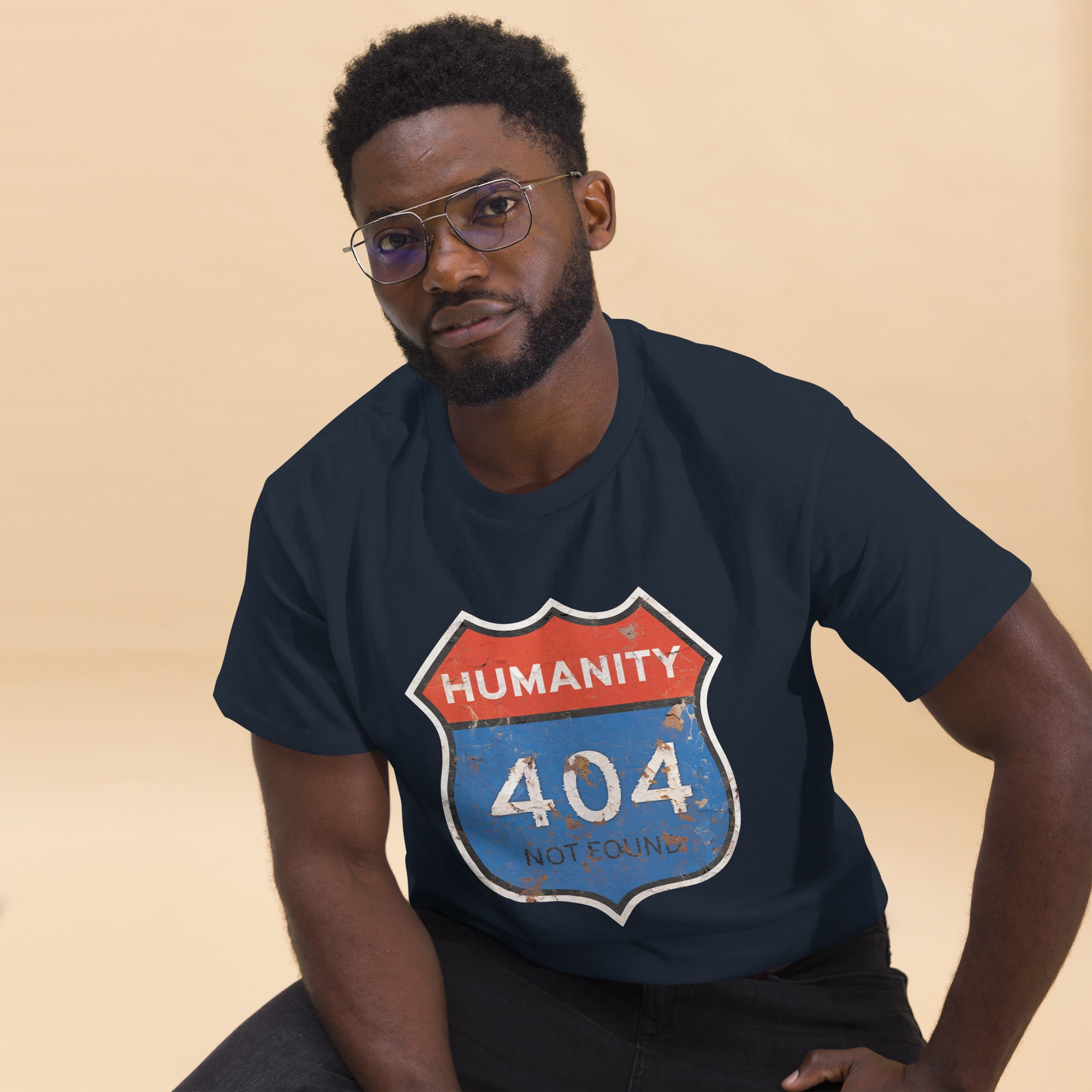 Man wearing a navy blue t-shirt with a 'Humanity 404 Not Found' graphic design on a beige background